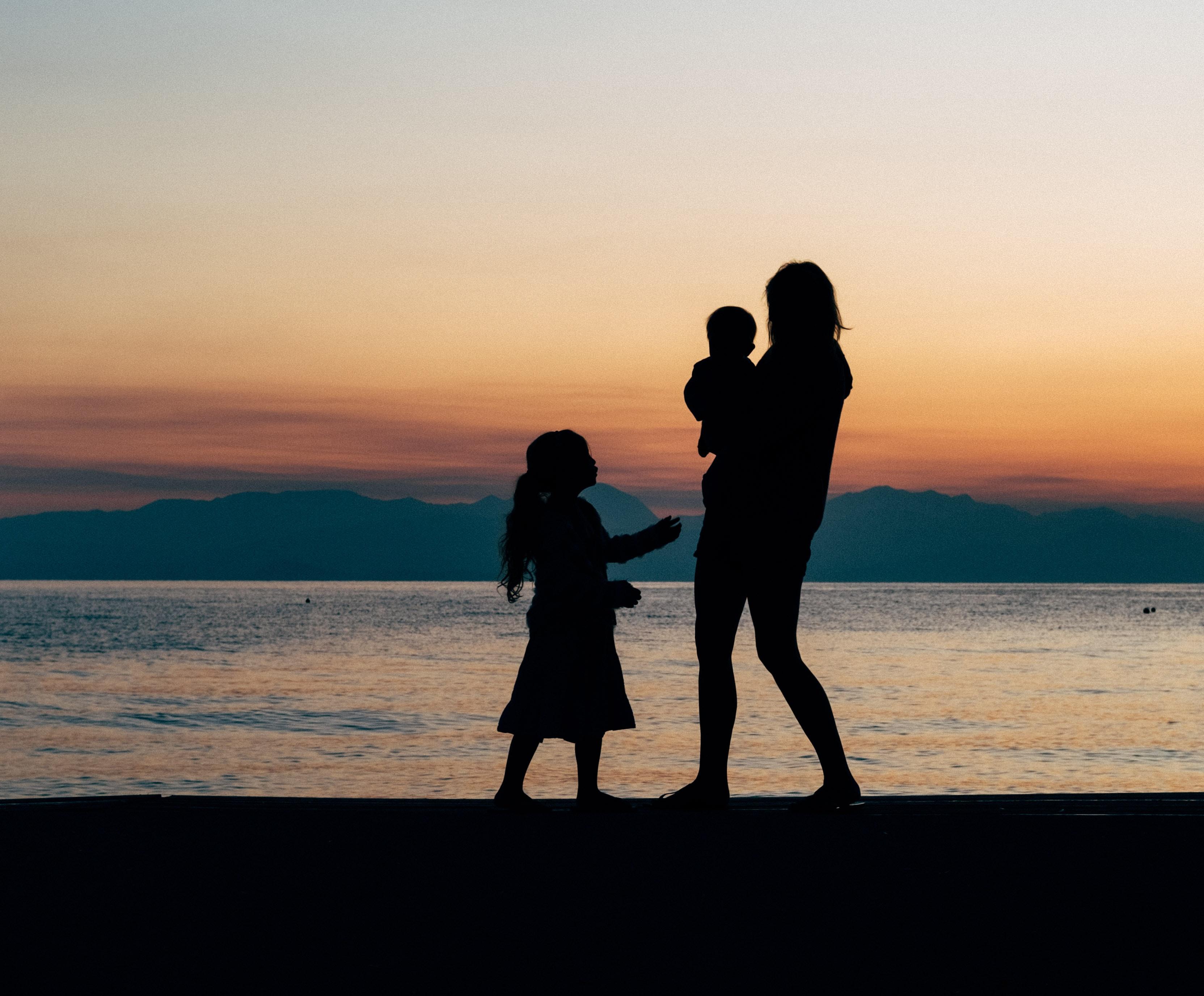 Silhouette of a mother and her children on a beach during a sunset.